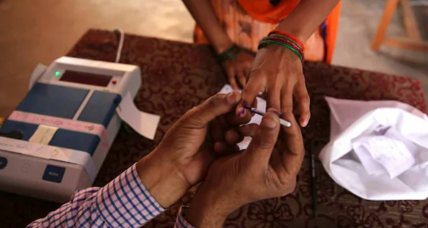 An election booth worker applies indelible to a voter's finger.