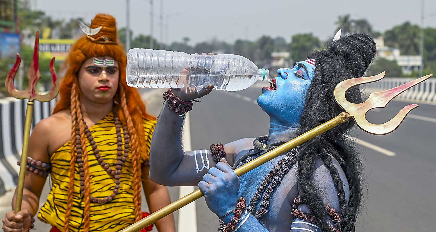 An artist dressed as Lord Shiva drinks water on a hot summer afternoon, in Nadia district