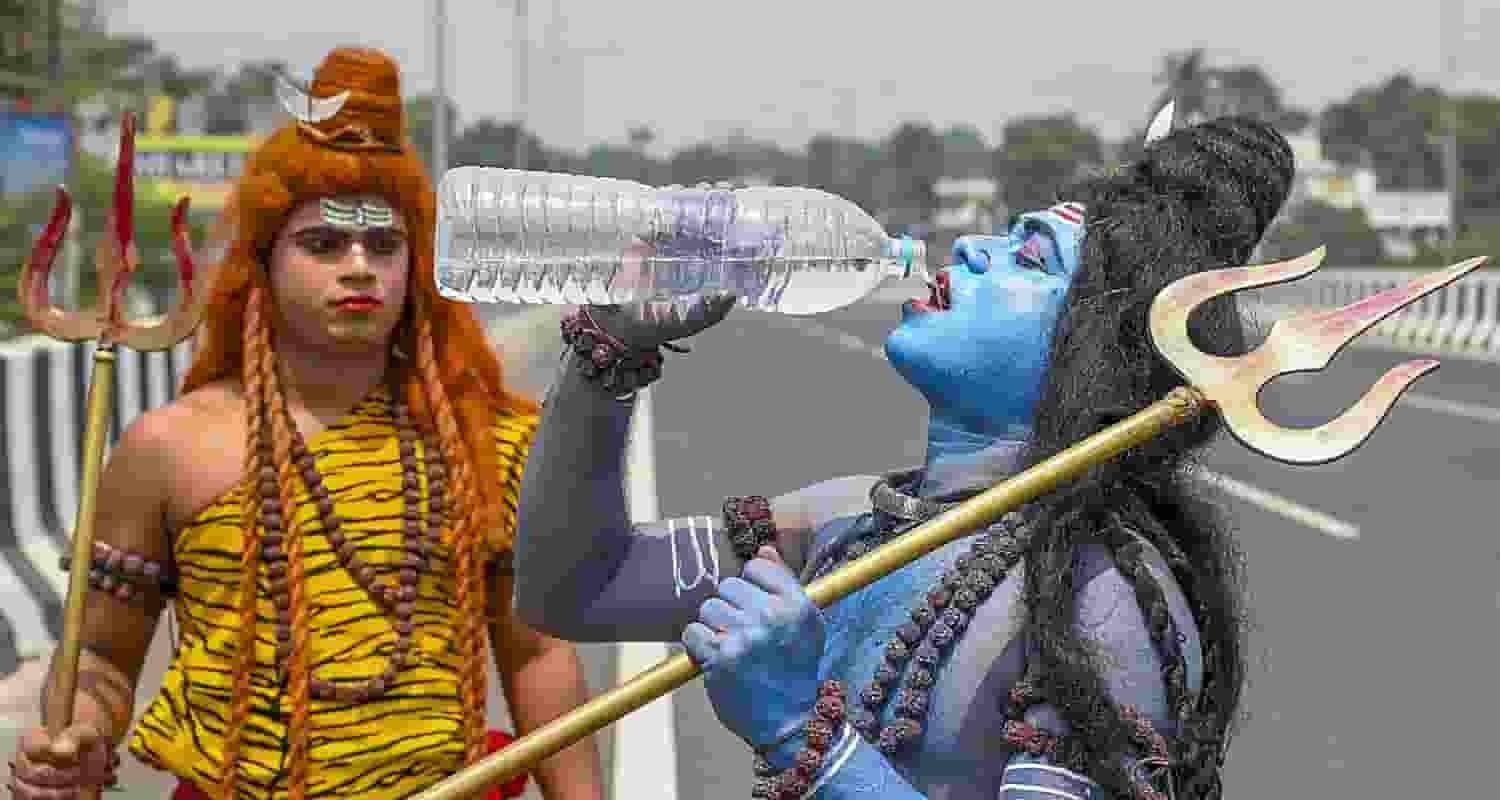 An artist dressed as Lord Shiva drinks water on a hot summer afternoon, in Nadia district